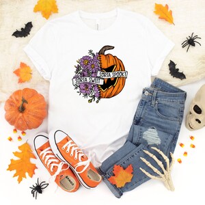May include: White t-shirt with a graphic of a pumpkin with flowers on one side and a jack-o-lantern face on the other. The text "Sorta Sweet" and "Sorta Spooky" is on a banner around the pumpkin.