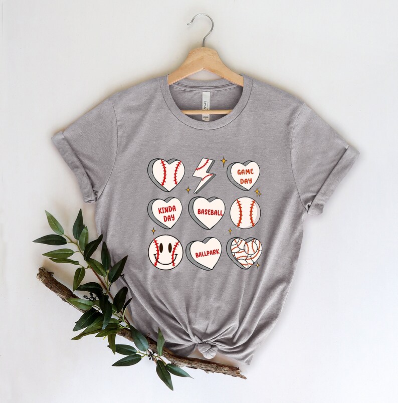 May include: Gray t-shirt with a baseball-themed design. The design features baseballs, hearts, and lightning bolts with text that says "Game Day", "Kinda Day", "Baseball", "Ballpark".