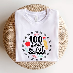 May include: White t-shirt with a black and red graphic that says "100 days of school" surrounded by black hash marks and colorful paper clips.