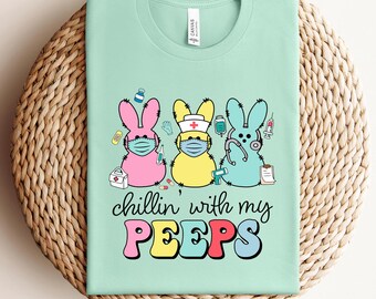 May include: A light green t-shirt with a graphic of three cartoon Peeps wearing face masks and holding medical supplies. The text "Chillin' with my PEEPS" is printed below the Peeps.