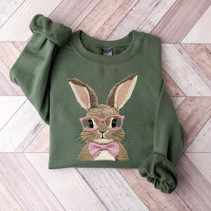 May include: A green sweatshirt with an embroidered image of a brown bunny wearing pink glasses and a pink bow tie.