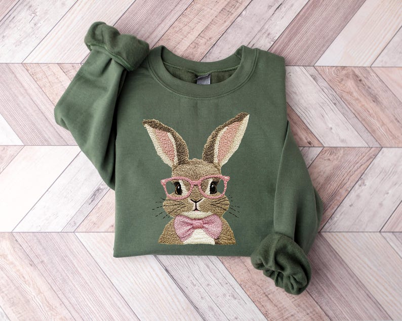 May include: A green sweatshirt with an embroidered image of a brown bunny wearing pink glasses and a pink bow tie.