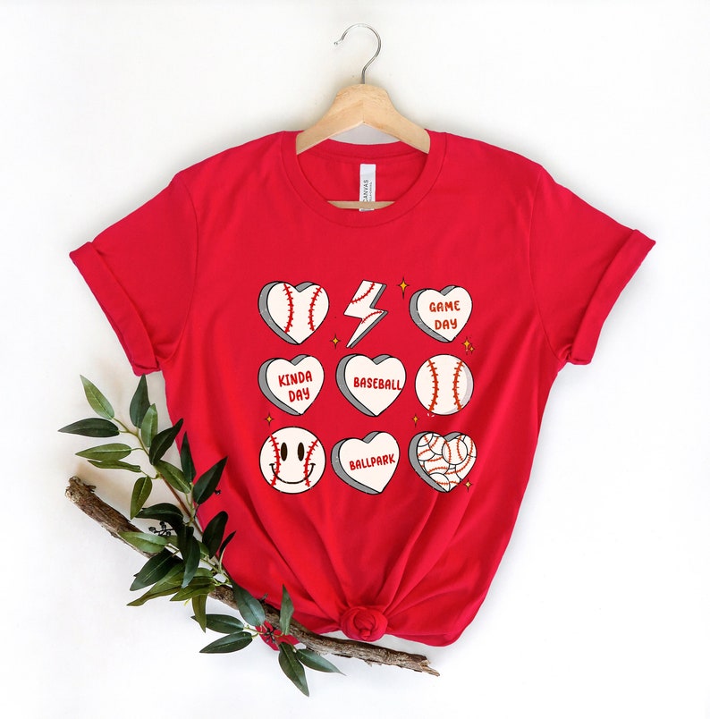 May include: Red t-shirt with a baseball-themed design. The design features baseballs, hearts, and phrases like "Game Day", "Kinda Day", and "Ballpark".