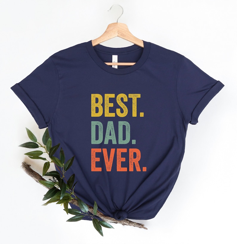 May include: Navy blue t-shirt with the text "BEST. DAD. EVER." in a vintage style font with yellow, orange, green, and red colors.