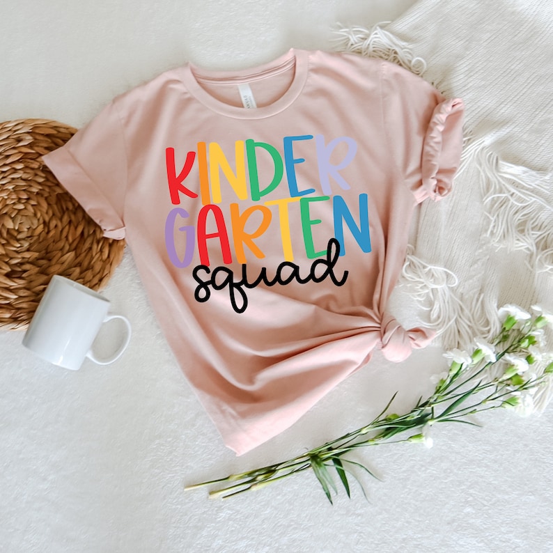 May include: A pink t-shirt with the text "Kindergarten Squad" in rainbow colors.