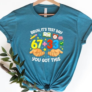 May include: Teal t-shirt with the text "Bruh, It's Test Day" and a math problem: 67 + 33. The design includes a pencil, book, clock, brain, and hands. The phrase "You Got This" is at the bottom.
