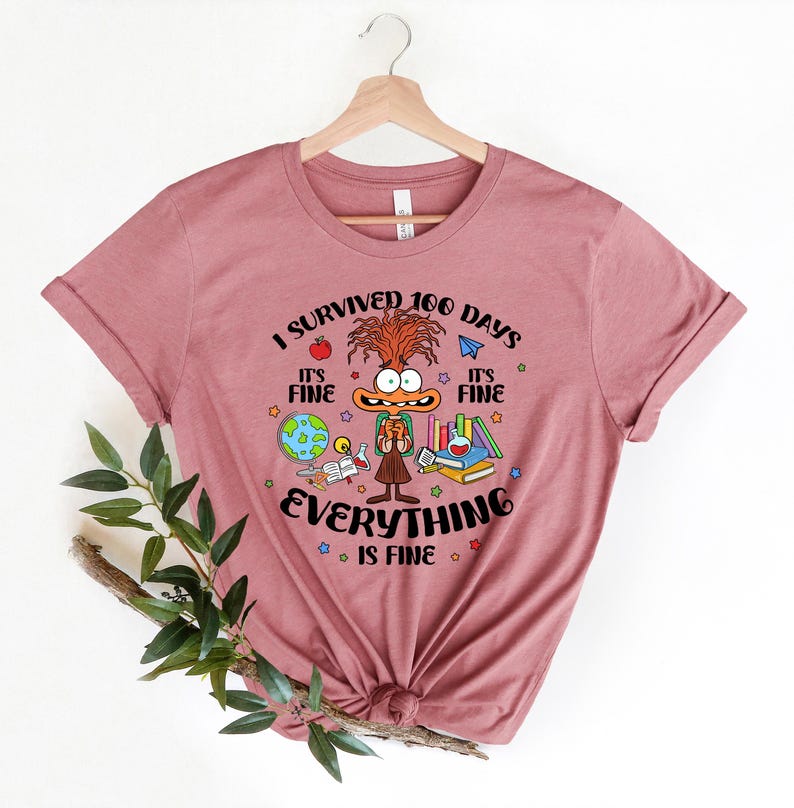 K&ouml;nnte beinhalten: Ein pinkfarbenes T-Shirt mit einer Comicfigur und dem Text "Ich habe 100 Tage &uuml;berlebt. Es ist in Ordnung. Alles ist in Ordnung."