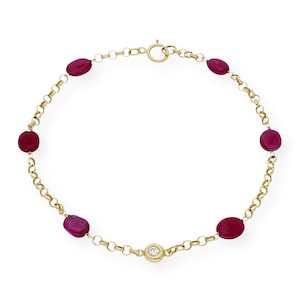 Op de afbeelding: Een gouden kettingarmband met rode ovale edelstenen en een enkele ronde, heldere edelsteen.