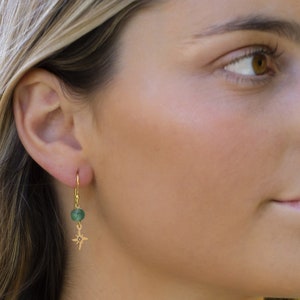 Puede incluir: Pendientes colgantes de oro con una piedra verde y un dije de estrella.