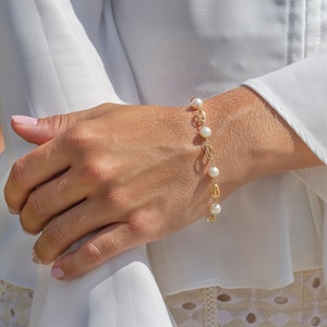 Könnte beinhalten: Ein goldenes Kettenarmband mit weißen Perlen. Das Armband befindet sich am Handgelenk einer Person.