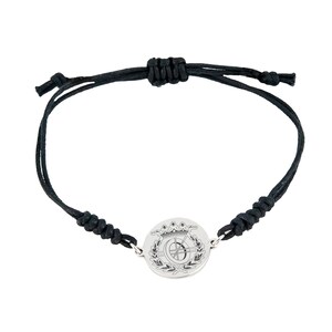 May include: A black cord bracelet with a silver circular charm featuring a crown and a letter C inside a wreath.
