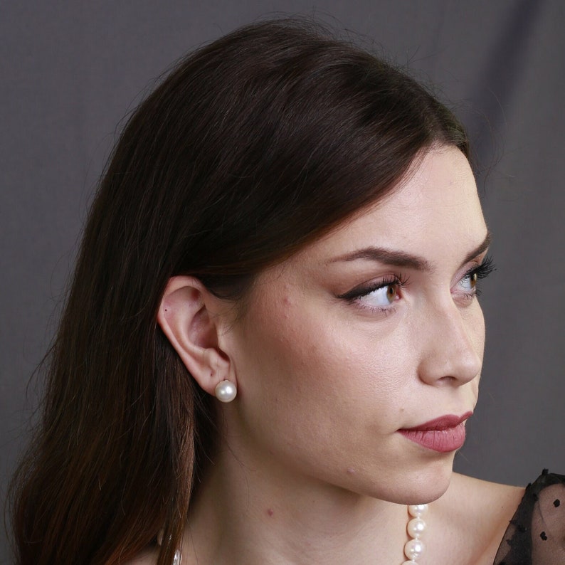 Puede incluir: Una mujer con el pelo largo y casta&ntilde;o que lleva un collar de perlas y pendientes de perlas. Lleva una blusa negra y mira hacia la derecha.