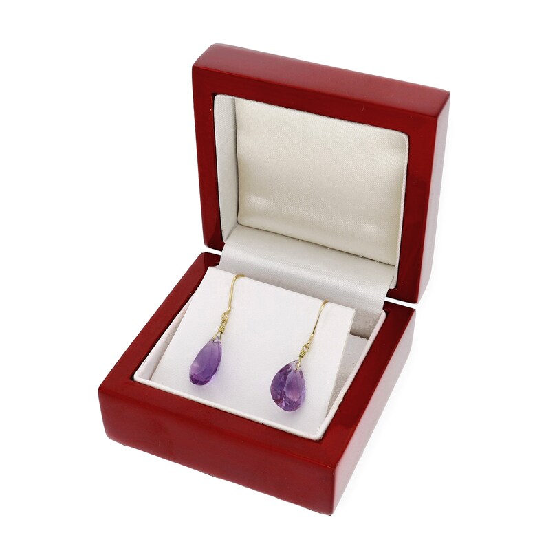 May include: A pair of amethyst drop earrings in a red jewelry box. The earrings are made of gold and have a teardrop-shaped amethyst gemstone.