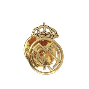 May include: A gold-colored metal pin featuring the Real Madrid crest with a crown on top. The crest is a circular design with a football inside and the letters "F.C.M." around the outside.