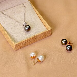 Puede incluir: Un conjunto de joyas de perlas que incluye un collar con un colgante de perla negra y un par de pendientes con perlas blancas y negras. El collar tiene un peque&ntilde;o racimo de diamantes sobre la perla.