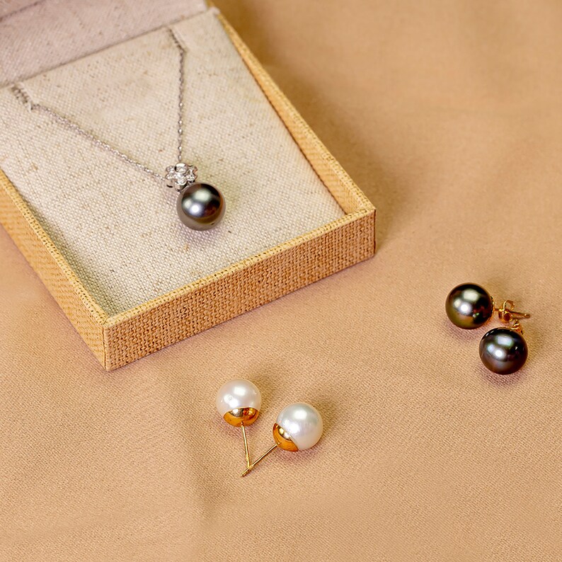 Puede incluir: Un conjunto de joyas de perlas que incluye un collar con un colgante de perla negra y un par de pendientes con perlas blancas y negras. El collar tiene un peque&ntilde;o racimo de diamantes sobre la perla.