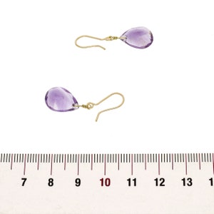 May include: A pair of gold earrings with teardrop-shaped amethyst stones. The earrings are approximately 1 inch long.
