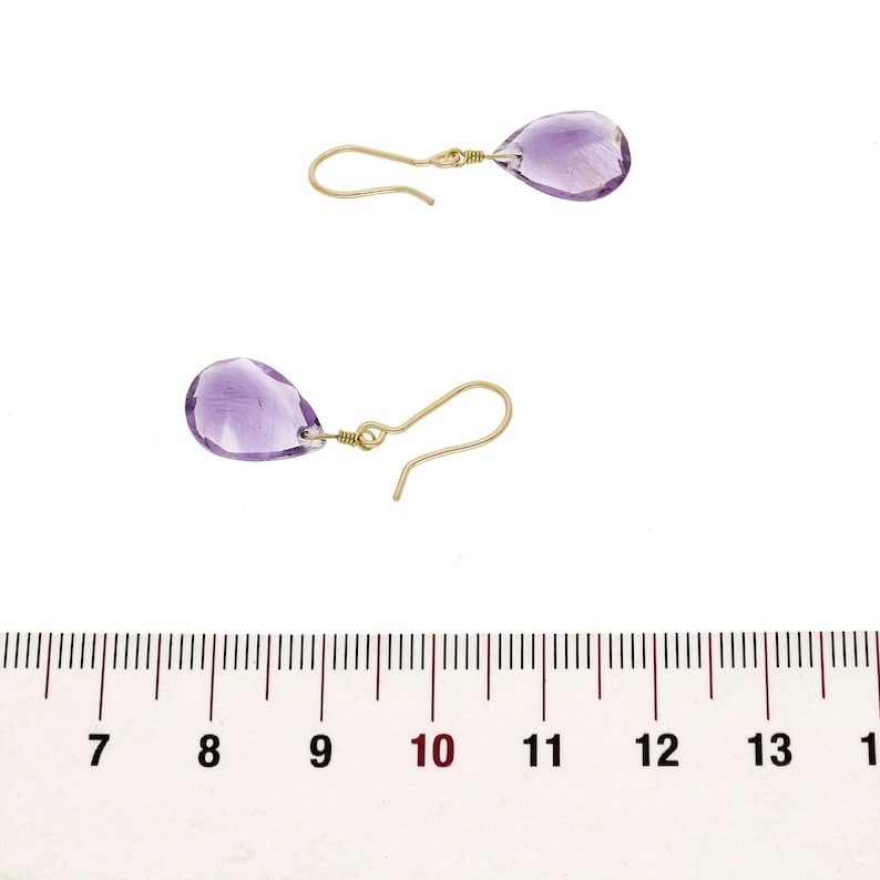May include: A pair of gold earrings with teardrop-shaped amethyst stones. The earrings are approximately 1 inch long.
