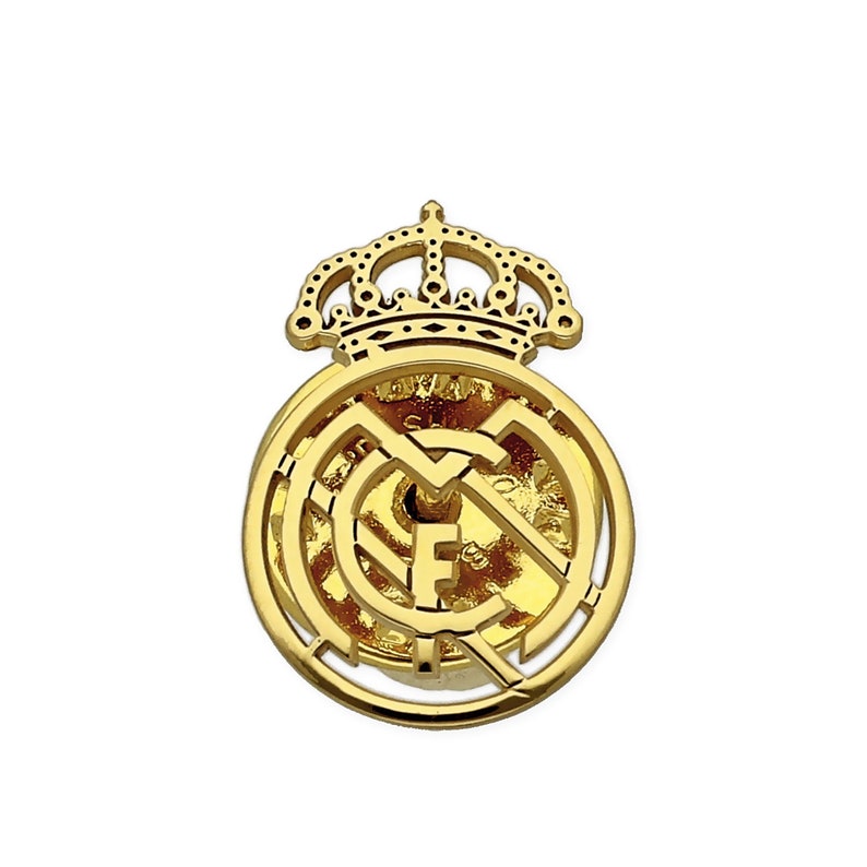May include: A gold metal pin with a crown and the Real Madrid crest. The crest features a white and gold design with a football in the center.