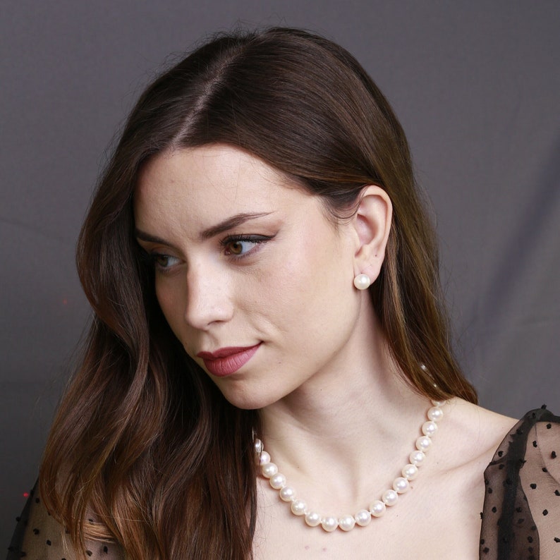 Puede incluir: Una mujer con el pelo largo y casta&ntilde;o que lleva un vestido negro con un collar de perlas y pendientes de perlas.