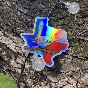 Peut inclure: Un autocollant holographique représentant un oiseau de dessin animé tenant une batte de baseball avec le texte "Austin, TX - June 2-3, 2023" et un contour de l'état du Texas.