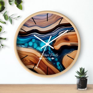 May include: A round wooden wall clock with a blue and brown abstract design. The clock face has white hands and black numbers. The text "The Johnson Family Established 2023" is printed on the clock face.