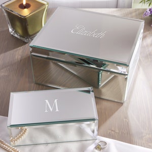 May include: Two mirrored jewelry boxes with a beveled edge. The larger box has the name "Elizabeth" engraved on the lid. The smaller box has the letter "M" engraved on the lid.