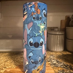 Puede incluir: Un vaso de acero inoxidable azul con un patr&oacute;n repetido de Stitch, el personaje extraterrestre de Lilo & Stitch, en varias poses. Stitch est&aacute; sosteniendo una guitarra, una rana y se muestra en otras poses juguetonas.
