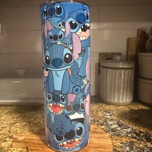 Puede incluir: Un vaso de acero inoxidable azul con un dise&ntilde;o de Stitch de Lilo & Stitch. El vaso est&aacute; cubierto de m&uacute;ltiples im&aacute;genes de Stitch en diferentes poses.