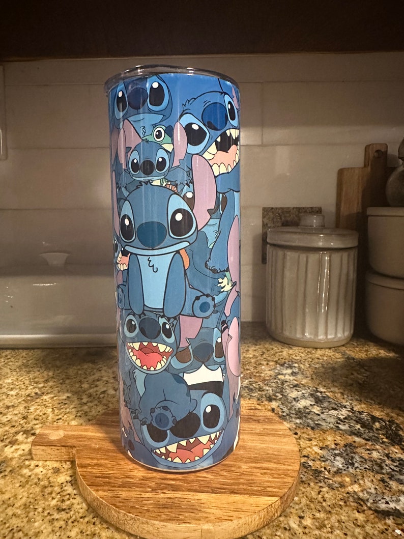 Puede incluir: Un vaso de acero inoxidable azul con un dise&ntilde;o de Stitch de Lilo & Stitch. El vaso est&aacute; cubierto de m&uacute;ltiples im&aacute;genes de Stitch en diferentes poses.