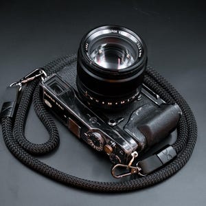 Könnte beinhalten: Schwarze Fujifilm X-Pro1 Kamera mit einem Super EBC Fujinon 1:2 f=35mm Objektiv und einem schwarzen geflochtenen Kameragurt. Der Gurt hat Lederakzente und Metallkarabiner. Das Objektiv ist 3,5 cm.