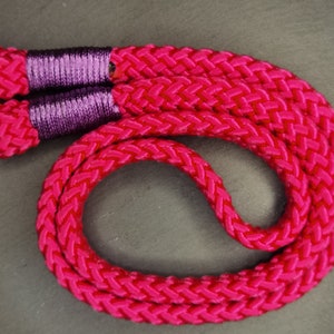 Op de afbeelding: Een roze gevlochten cameraband met paarse accenten en metalen ringen.