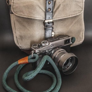 Può includere: Una macchina fotografica nera con una tracolla verde e arancione e una borsa per fotocamera in tela grigia.