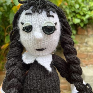 Peut inclure: Poupée tricotée à la main avec des tresses en fil noir, un visage blanc et une robe noire. La poupée a des yeux en boutons et un col blanc. Les cheveux de la poupée sont coiffés en deux longues tresses.