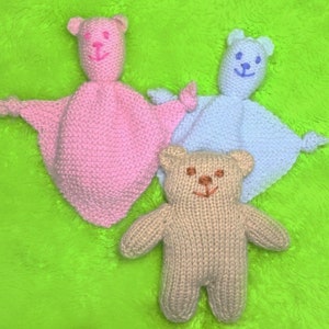 May include: Three knitted teddy bears, one pink, one light blue, and one beige. The pink and blue bears are lying down with their arms outstretched, while the beige bear is standing upright with its arms at its sides.