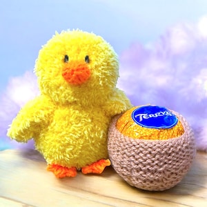 Peut inclure: Un jouet en peluche jaune et duveteux en forme de poussin à côté d'un œuf en chocolat enveloppé dans une couverture en tricot marron. L'œuf en chocolat porte une étiquette bleue avec le mot "Terry's" dessus.