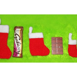May include: Four red and white knitted Christmas stockings of varying sizes, a chocolate bar, and a gift card. The stockings are filled with candy.