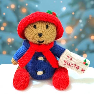 May include: A handmade knitted teddy bear wearing a red hat and scarf, a blue coat, and red boots. The bear holds a white envelope with "To Santa X". A festive Christmas decoration.