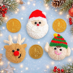 May include: Three crocheted Christmas ornaments featuring a Santa Claus head with a red hat, a reindeer head with a red nose, and an elf head with a green and red striped hat, arranged with three gold-coloured chocolate coins on a blue background.