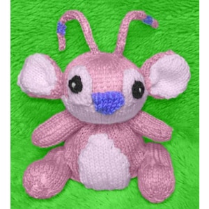 Peut inclure: Un jouet en peluche rose tricoté avec des accents bleus. Le jouet a de grandes oreilles, un petit nez et deux antennes avec des fleurs bleues sur le dessus.