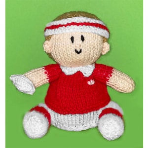 May include: A knitted doll wearing a red and white outfit with a white headband. The doll has a smiling face and is sitting on a green background.