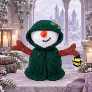 May include: A crocheted snowman doll wearing a dark green hooded cloak with a small holly leaf accent. The snowman has a white textured head, a bright orange nose, and black bead eyes and mouth. It has brown twig-like arms and holds a small yellow and black striped ornament.