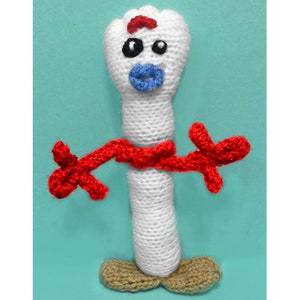 May include: White crocheted toy with a red scarf and blue eyes. The toy has a red mouth and a white body. The toy is standing on a brown base.