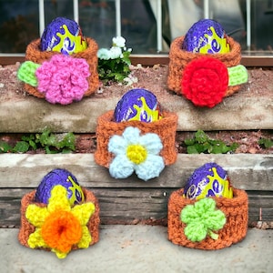 May include: Five crocheted Easter egg holders with different colored flowers and a shamrock design. Each holder features a purple foil-wrapped chocolate egg.