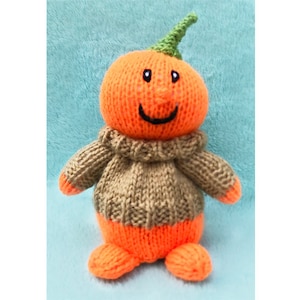 May include: A knitted orange pumpkin with a green stem and a brown sweater. The pumpkin has a smiling face with black eyes and a mouth.