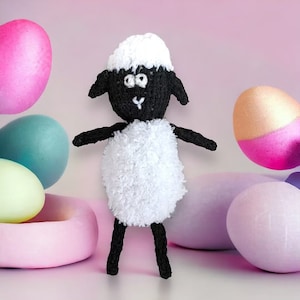 May include: A black and white knitted sheep toy with a fluffy white body and black face. The sheep has large black eyes and a small black nose. The toy is surrounded by pastel coloured Easter eggs.