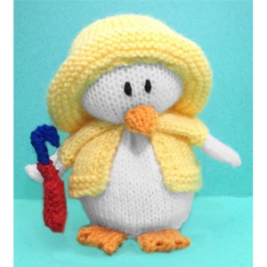 May include: A white knitted penguin wearing a yellow knitted raincoat and holding a red and blue umbrella.