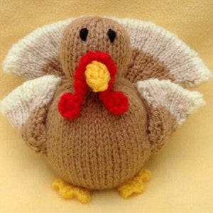 May include: A knitted brown turkey with a red wattle and yellow beak. The turkey has white and brown feathers on its wings.