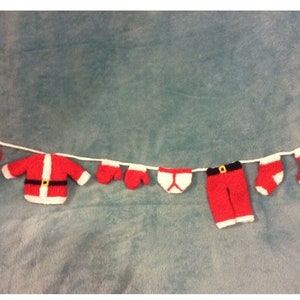 May include: A string of knitted Christmas ornaments, including a Santa suit, mittens, underwear, pants, and socks, hanging on a white string.