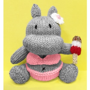 May include: A gray knitted hippopotamus wearing a pink bikini and holding a red, white, and brown ice cream cone. The hippopotamus has a white flower on its head.